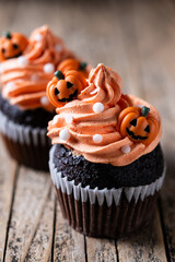 Halloween cupcakes with pumpkin decoration on rustic wooden table and black background
