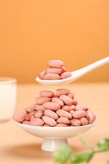 Raw Peanuts Kernels in White Bowl with Spoon on Orange Background