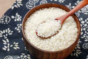 Pearl Rice Grains in Wooden Bowl with Spoon on Traditional Asian Pattern Cloth