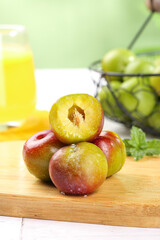 Premium fresh red plums chopped in half showing flesh on wooden board with juice