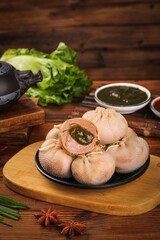 Traditional Mongolian Steamed Buns with Savory Filling and Dipping Sauce on Wooden Board