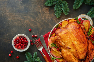 Christmas roasted chicken with apples, potatoes, cranberries, sauce and herbs on large plate on old dark marble background. Festive family poultry dish. Top view. Copy space.