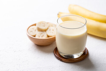 Banana milk in glass with sliced banana and fruit on white background