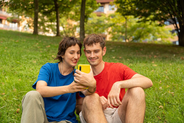 Young couple sitting on grass using smartphone in park