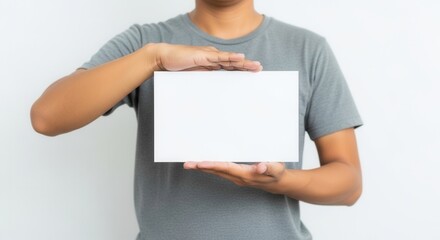 A person in a grey short-sleeved top holds a plain white rectangular sheet with both hands against a light background