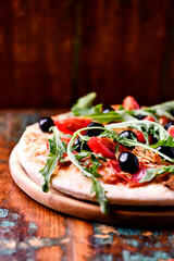 Pizza with ham, salami, tomatoes and mozzarella cheese. Rustic wooden background. Soft focus. Close up.	