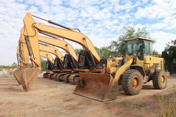 Lots of excavators parked on construction area of industrial building in construction site under the blue sky background.Earthmoving construction equipment