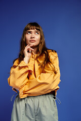 Stylish young woman poses thoughtfully against a vibrant blue background