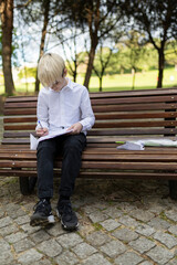 Elementary school student doing homework outdoors on park bench