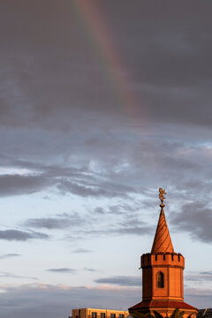 Oberbaum Bridge tower in Berlin with rainbow above dramatic evening sky, historic red brick landmark symbolizing cultural heritage and connection across Spree River