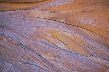 Obraz premium textured multicolored sand surface at abandoned kaolin mine, the patterns resemble streaks of natural sediment layers, creating a dynamic, abstract visual effect.