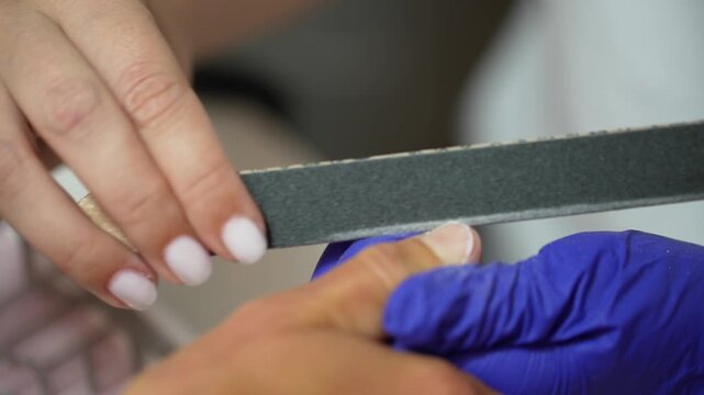 Close-up of professional manicurist filing client nail with emery board, beauty salon nail care video concept.
