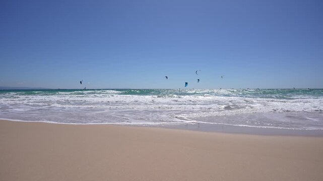 Tarifa, Spain &ndash; View of sandy beach with ocean waves and kitesurfers in the sky.