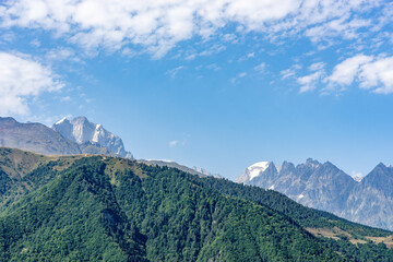Majestic mountain peak towering over lush green forest in Georgia under a cloudy blue sky © klenger