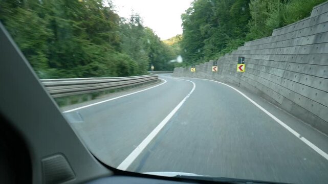 POV video from the driver&rsquo;s seat during a car ride through winding mountain roads in Romania. The route features sharp turns marked by numerous traffic signs and a distinctive stone retaining wall
