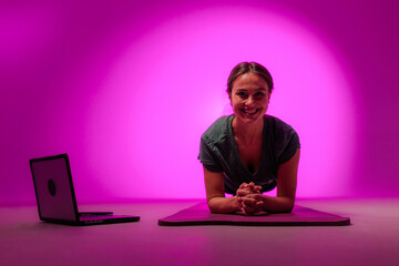 Fitness trainer doing online plank exercise in studio with purple background
