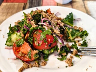 Fresh salad with tomatoes cucumbers onions herbs and ground walnuts on a white plate closeup view