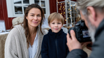 A cheerful woman and a young boy pose together for a photo in a festive outdoor setting filled with holiday decorations and warm ambiance, capturing shared moments of joy.