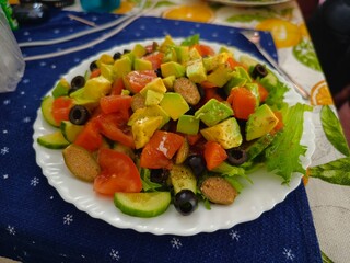 Fresh avocado salad with tomatoes cucumbers and black olives on a white plate for a healthy meal