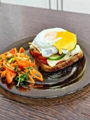 Delicious open faced sandwich with a fried egg and a side salad on a dark plate sitting on a table