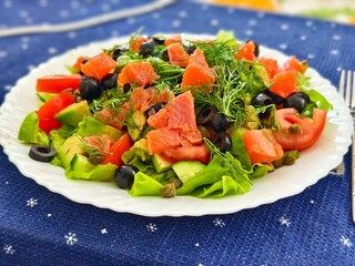 Fresh salmon salad with avocado tomatoes olives and dill on a white plate ready to be served