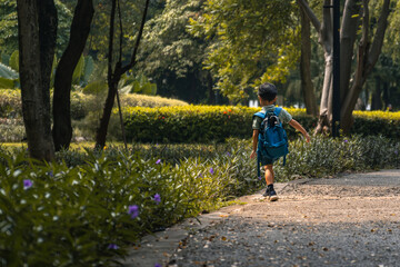 Obraz premium young child with a blue backpack walking along a peaceful park pathway surrounded by trees and greenery