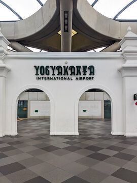 Traditional Javanese gapura gate welcomes travelers at an airport terminal, blending ornate white arches with modern architecture and patterned tile flooring in Yogyakarta, Indonesia.