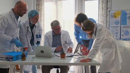 Group of doctors in lab coats actively debating medical research and scientific reports. Senior physician leads discussion on suitability of new drugs. Team studies data and clinical papers in office. - Powered by Adobe