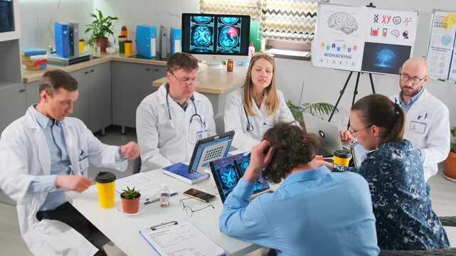 Group of doctors and medical interns in white coats exchange documents and reports during a clinical meeting. Professional discussion, teamwork, research papers and healthcare collaboration in