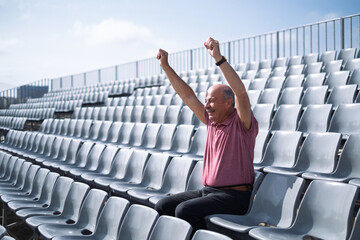 elderly man sitting alone at stadium cheering for his team, celebrating a goal