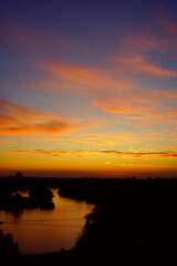 Scenic sunset over the Danube: colorful sky with clouds, water of river, the silhouette of the Genex Tower and other buildings in the New Belgrade area. Harmony between the city and natural beauty