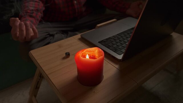 Close up meditation ritual at home, hands in mudra with laptop guided audio and evening candlelight
