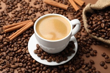 Cup of hot coffee, beans and cinnamon on brown background, closeup