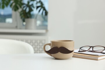 Happy Father's Day. Cup with paper moustache, books and glasses on white table indoors, space for text