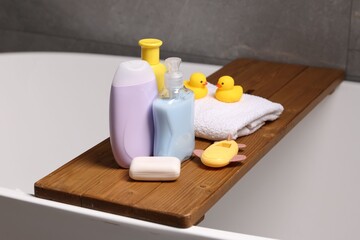 Baby accessories and bathing products on wooden tray in bathtub indoors, closeup