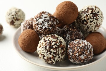 Tasty chocolate candies with cocoa powder, nuts and sesame seeds on white table, closeup