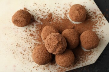 Tasty chocolate candies with cocoa powder on black table, top view