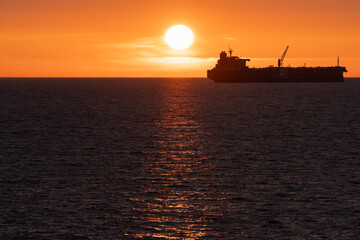 Majestic Silhouette of a Large Tanker Ship Navigating the Serene Waters of the Baltic Sea at Sunset, with the Golden Sun Descending Over the Estonian Coastline.