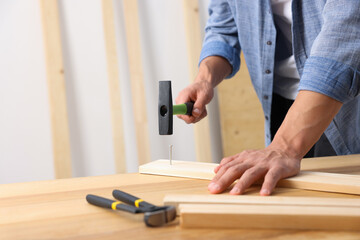 Man hammering nail into wooden plank indoors, closeup. Space for text