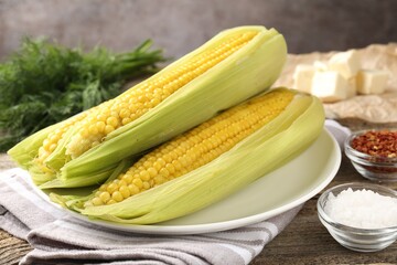 Tasty boiled corncobs, dill and spices on wooden table, closeup