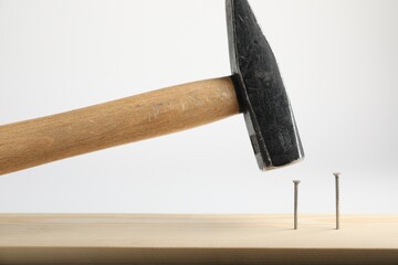 Hammering nail into wooden plank on white background, closeup