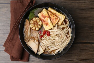 Tasty ramen with enoki and king oyster (eryngii) mushrooms in bowl on wooden table, top view