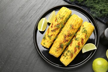 Tasty grilled corncobs with dill and lime slices on black table, flat lay