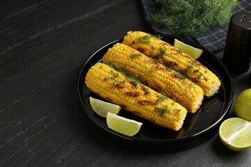 Tasty grilled corncobs with dill and lime slices on black table. Space for text