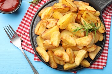 Tasty baked potatoes with rosemary and ketchup served on light blue wooden table, flat lay