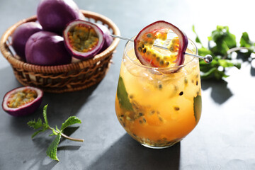 Tasty passion fruit drink in glass, fresh fruits and mint on gray table, closeup