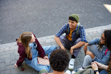 Happy teenager friends sitting and chatting together outdoors
