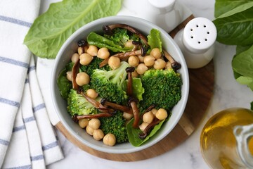 Delicious salad with shimeji mushrooms, chickpeas and broccoli in bowl on white marble table, flat lay