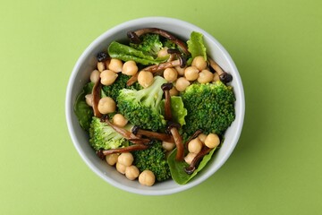 Delicious salad with shimeji mushrooms, chickpeas and broccoli in bowl on green background, top view