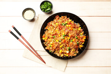 Tasty fried rice and chopsticks on light wooden table, flat lay